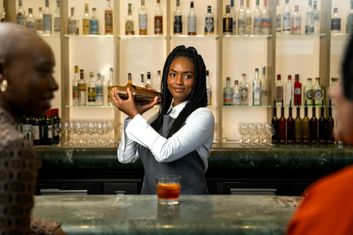 A bartender shaking a cocktail behind a green-topped bar