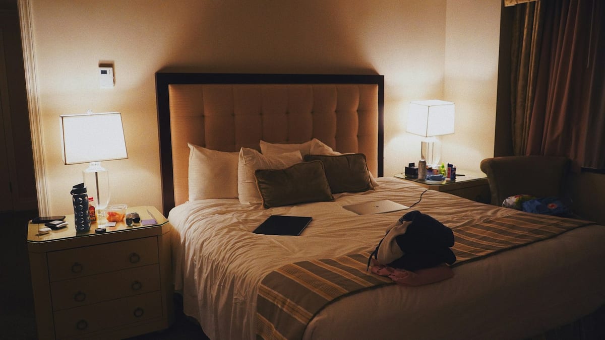 A hotel bedroom with the bedside lamps lit, a guest's bag on the bed