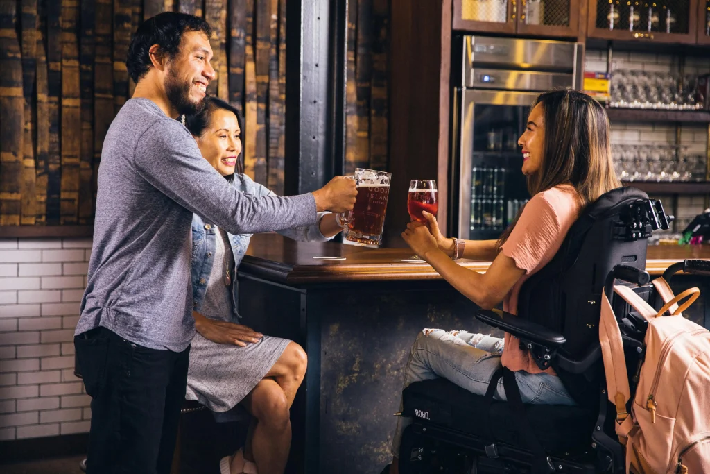 Smiling patrons toasting drinks at a bar, illustrating the success that comes from thriving in the hardest in hospitality roles.