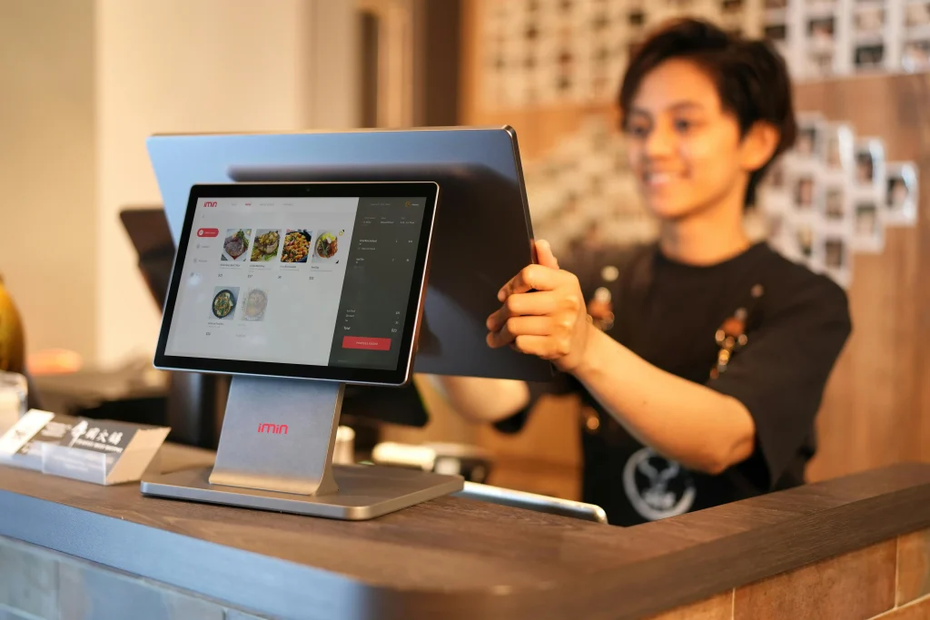 A smiling front-of-house employee using a touchscreen system, contemplating which country pays the best in hospitality.