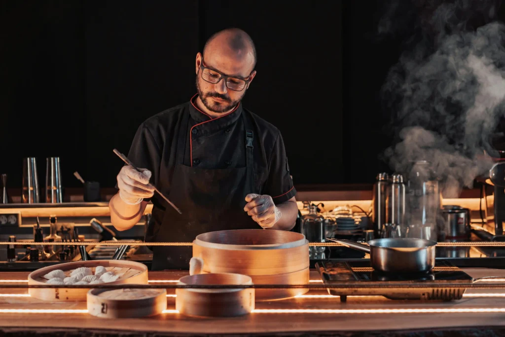A head chef carefully preparing a dish in a smoky kitchen, exemplifying one of the hardest in hospitality roles.