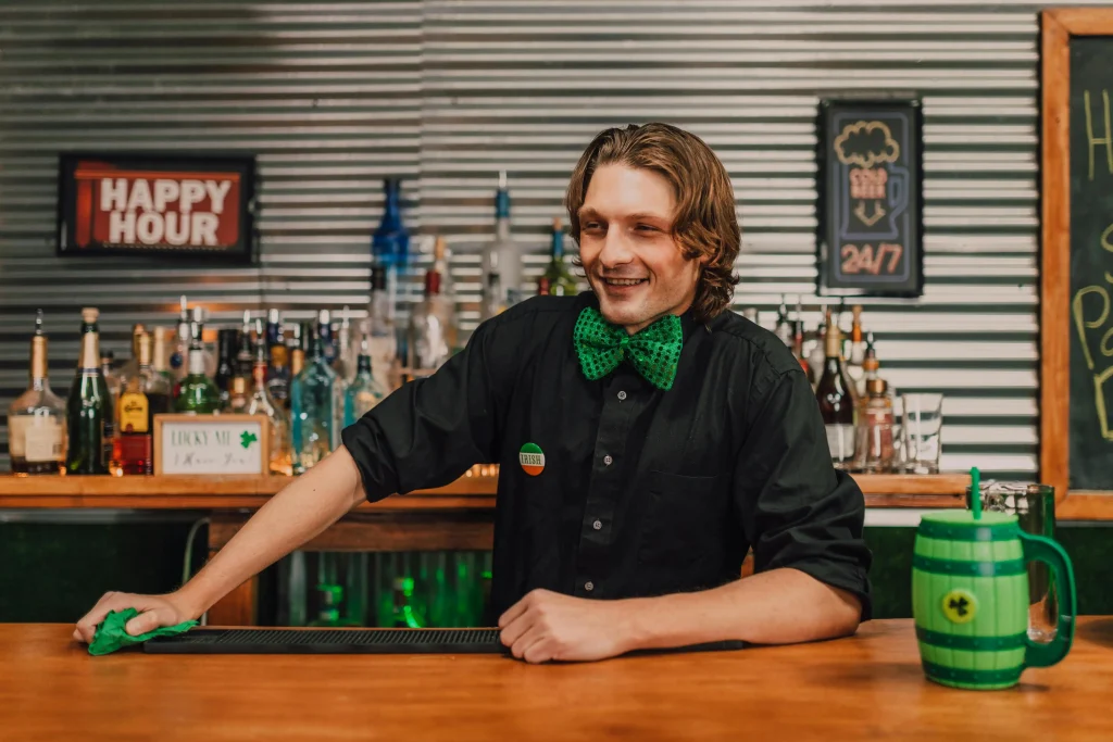 A smiling bartender serving drinks at a lively bar, representing front-of-house roles and key jobs in hospitality.