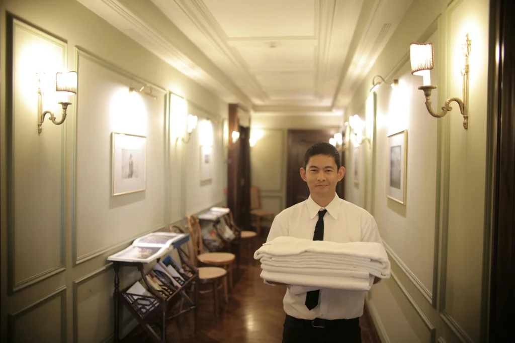 Hospitality trainee holding neatly folded towels in a luxury hotel corridor during a training program in London.